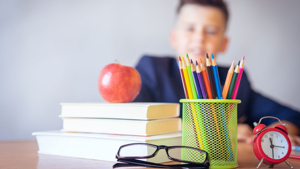 Skolböcker och pennor på skrivbord med pojke i bakgrunden