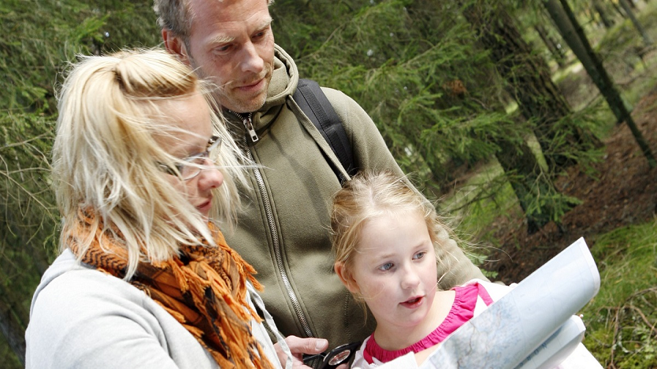 Föräldrar med barn på vandring i natur och karta i handen