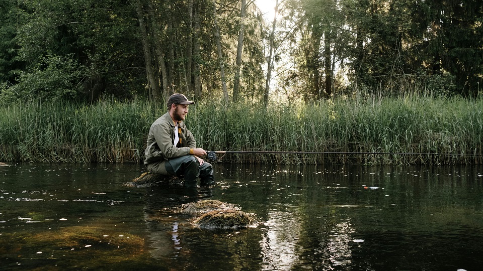 En man sitter och fiskar på en sten i vattnet
