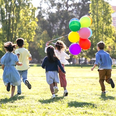 Barn som springer med färgglada ballonger över en gräsmatta en solig dag