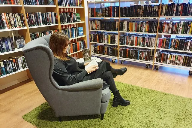 Kvinna sitter i fåtölj i deckarhörnet på biblioteket