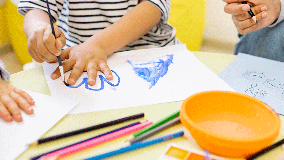 Händer som målar och vattenfärger i olika kulörer.