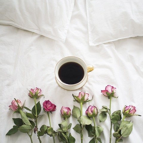 Rosa rosor och en kaffekopp på en säng med vita lakan