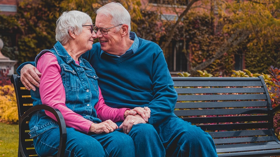 Ett äldre par som sitter på en parkbänk och håller om varann.