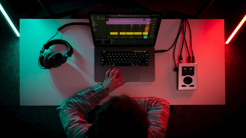 Person sitter vid datorn och skapar musik.