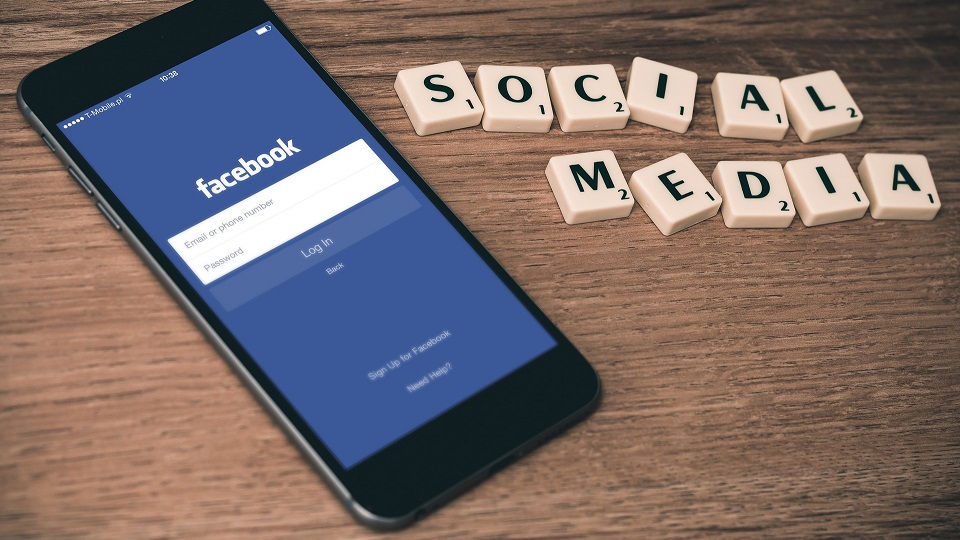 en mobil med en bild på Facebook och bredvid ligger det bokstäver som bildar orden sociala medier