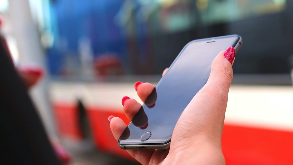 Hand håller mobiltelefon framför buss