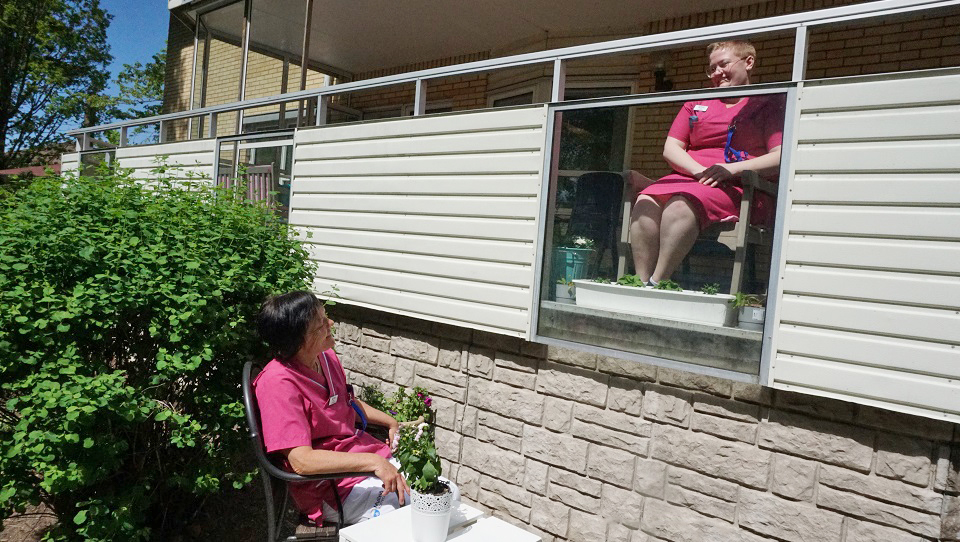 Kvinna sitter på balkong, nedanför sitter annan kvinna på behörigt avstånd.