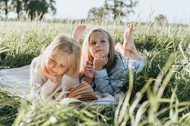 Två barn ligger i gräset och läser böcker.