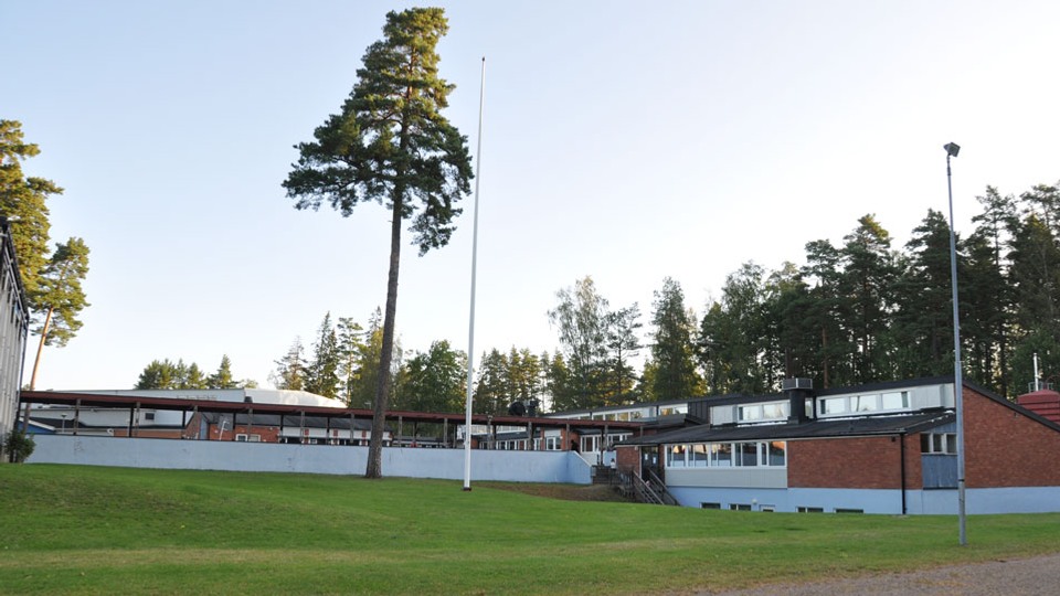 Skolbyggnad i rött tegel med gräsplan framför