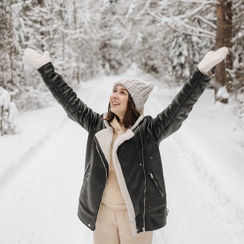 En leende kvinna som sträcker sina händer mot himlen  i förgrunden till ett vinterlandskap.