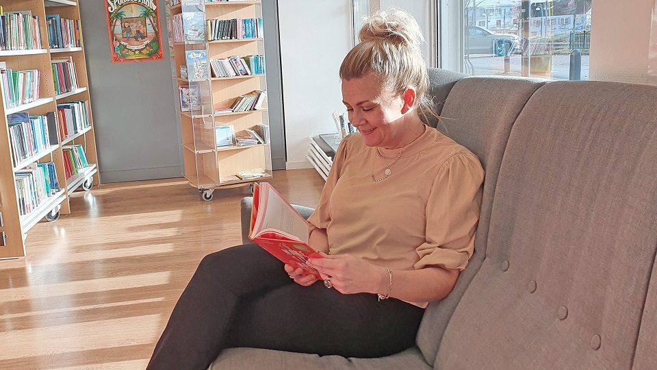 Kvinna sitter i soffan på biblioteket och läser i en bok.