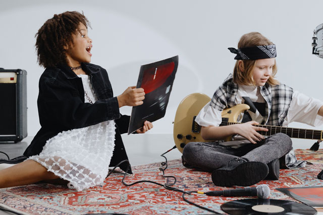 Två barn sitter på golvet med gitarr och LP-skivor om kring sig