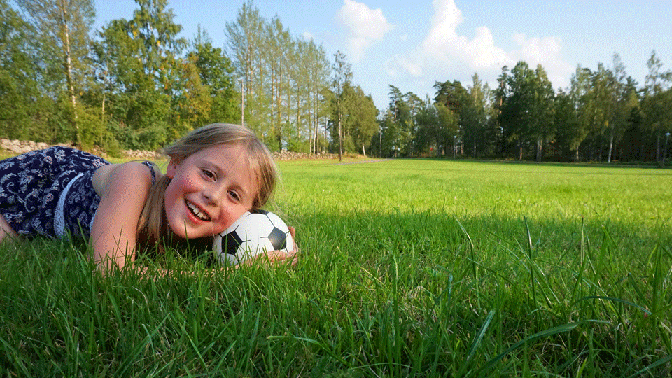 Glad tjej ligger på gräsmatta med fotboll som huvudstöd