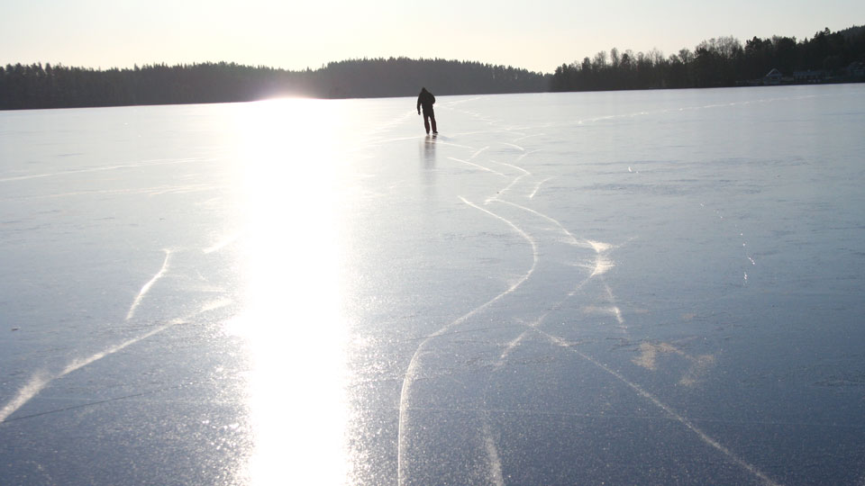 Man åker långfärdsskridskor på is i solnedgång