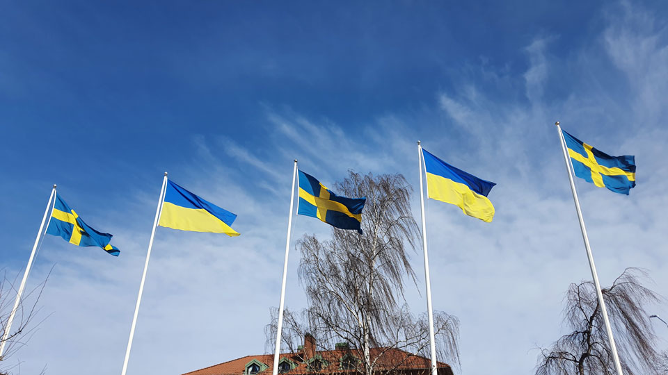 Fem flaggor i vinden. Svenska flaggor på ytterkanter och i mitten och ukrainska flaggor däremellan