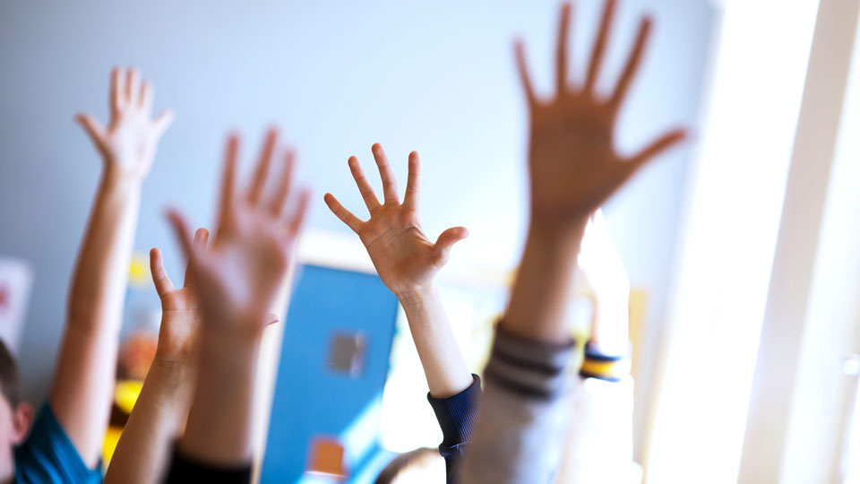 Skolbarn som räcker upp sina händer i ett klassrum