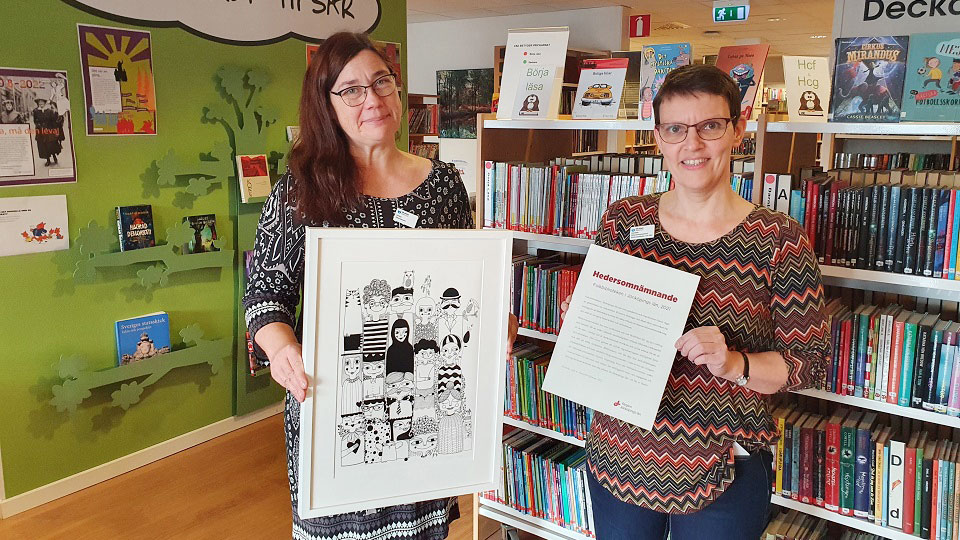 Bibliotekspersonalen håller upp hedersomnämnandet och ett grafiskt konstverk som de fått.