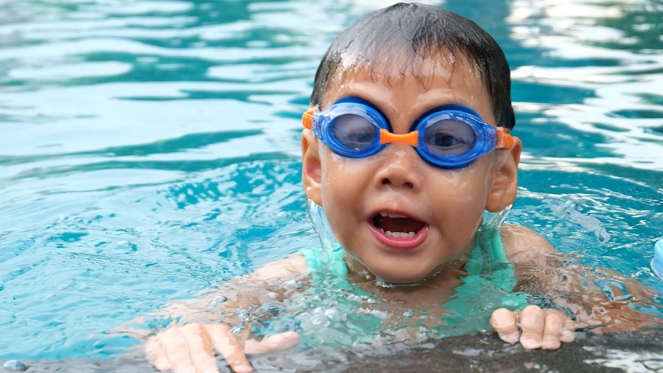 Liten pojke med simglasögon hänger vid poolkanten