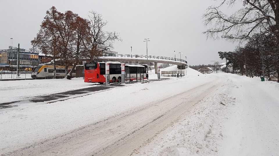 Vinterväg som plogats, tåg och buss i bakgrunden