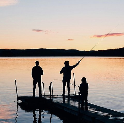 Tre människor står på en brygga och fiskar i solnedgång