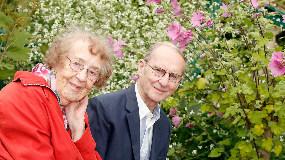 Äldre par sitter tillsammans i trädgård.
