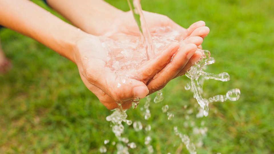 Bild på händer som tvättas i rinnande vatten utomhus. 