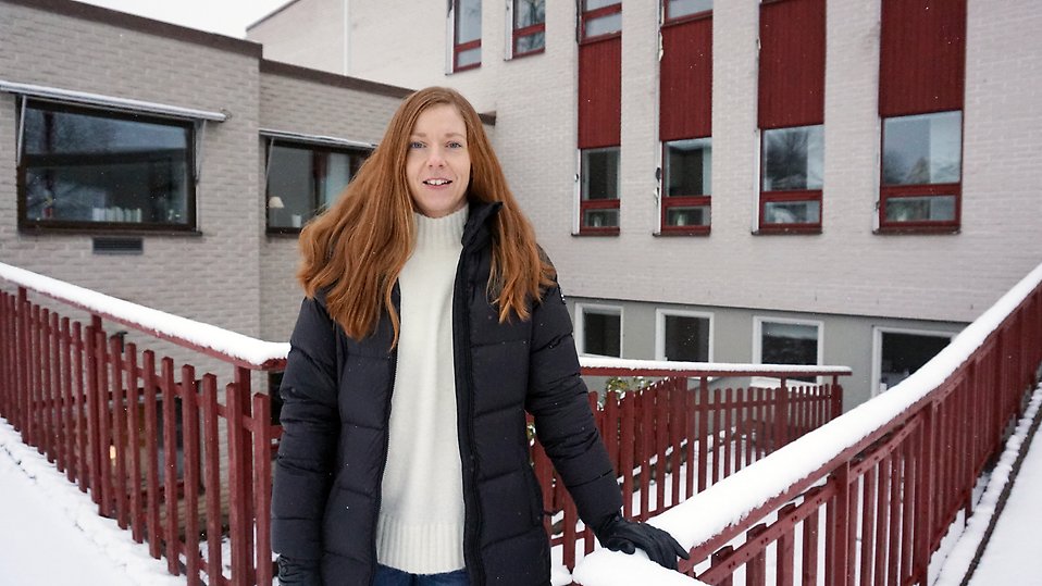 Kvinna står i vinterkläder  en kall vinterdag vid en byggnad